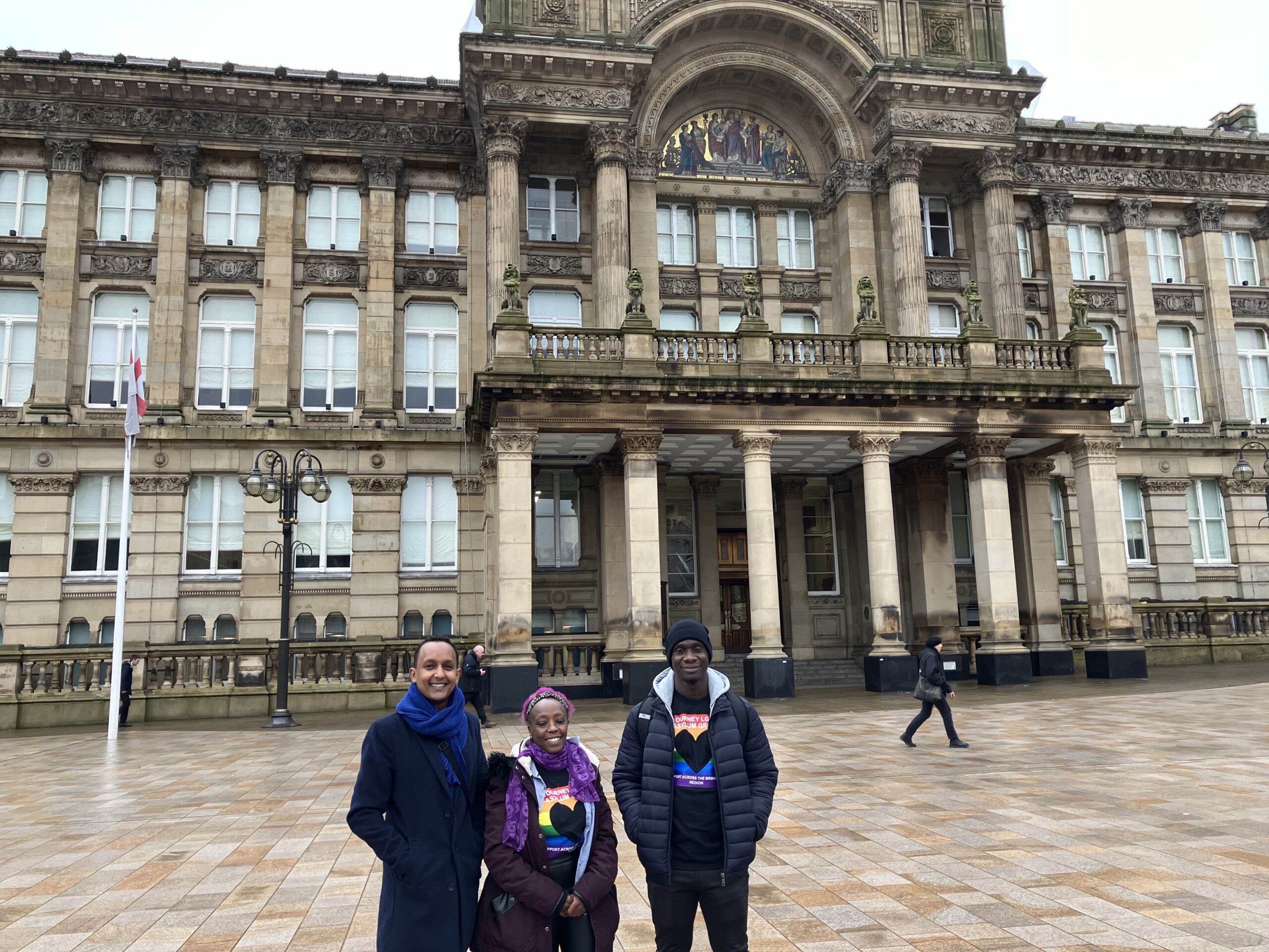 Three Journey members standing smiling at the camera in front of Birmingham City Council House