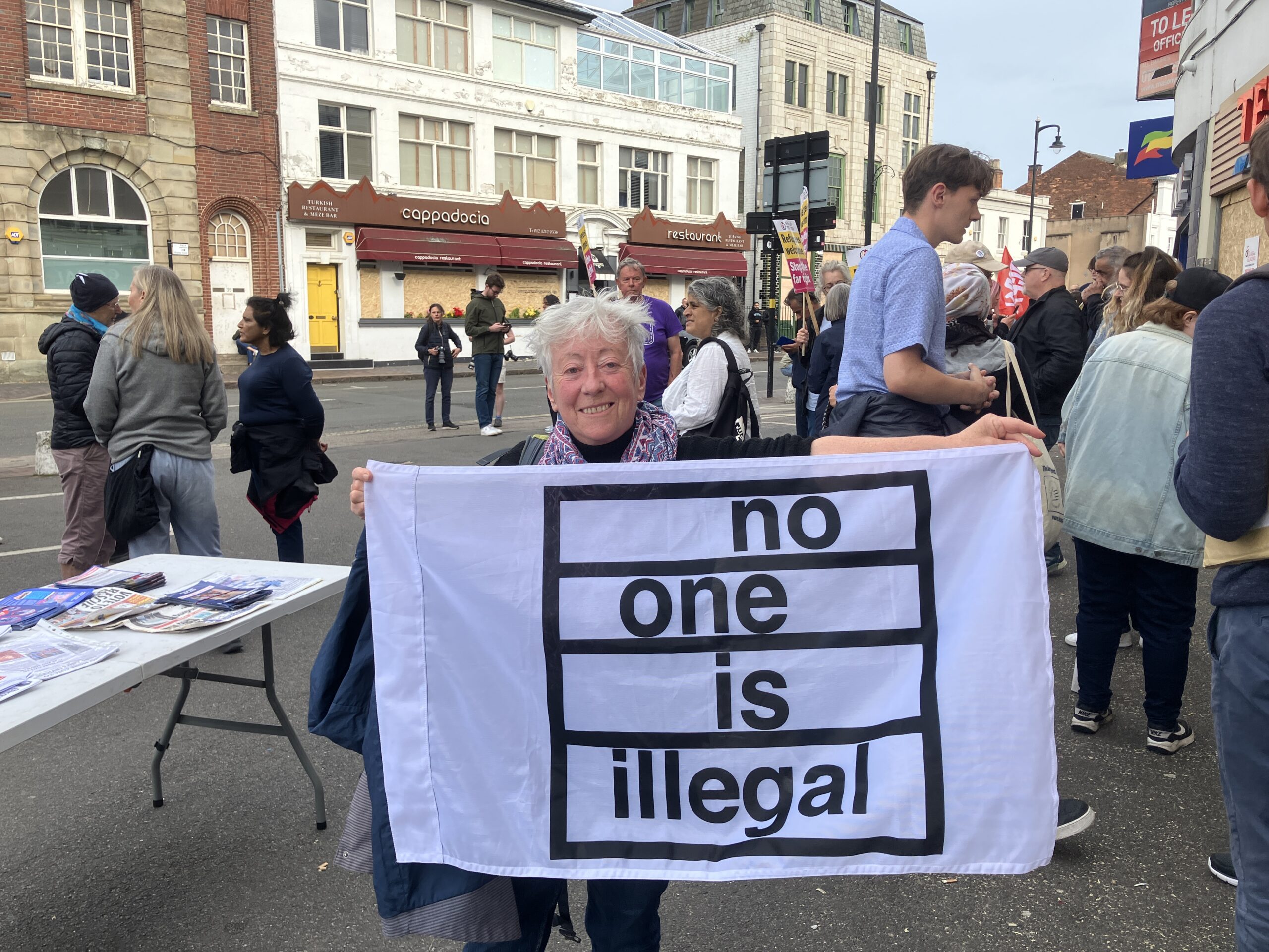 Sheila holding a banner saying 'no one is illegal'